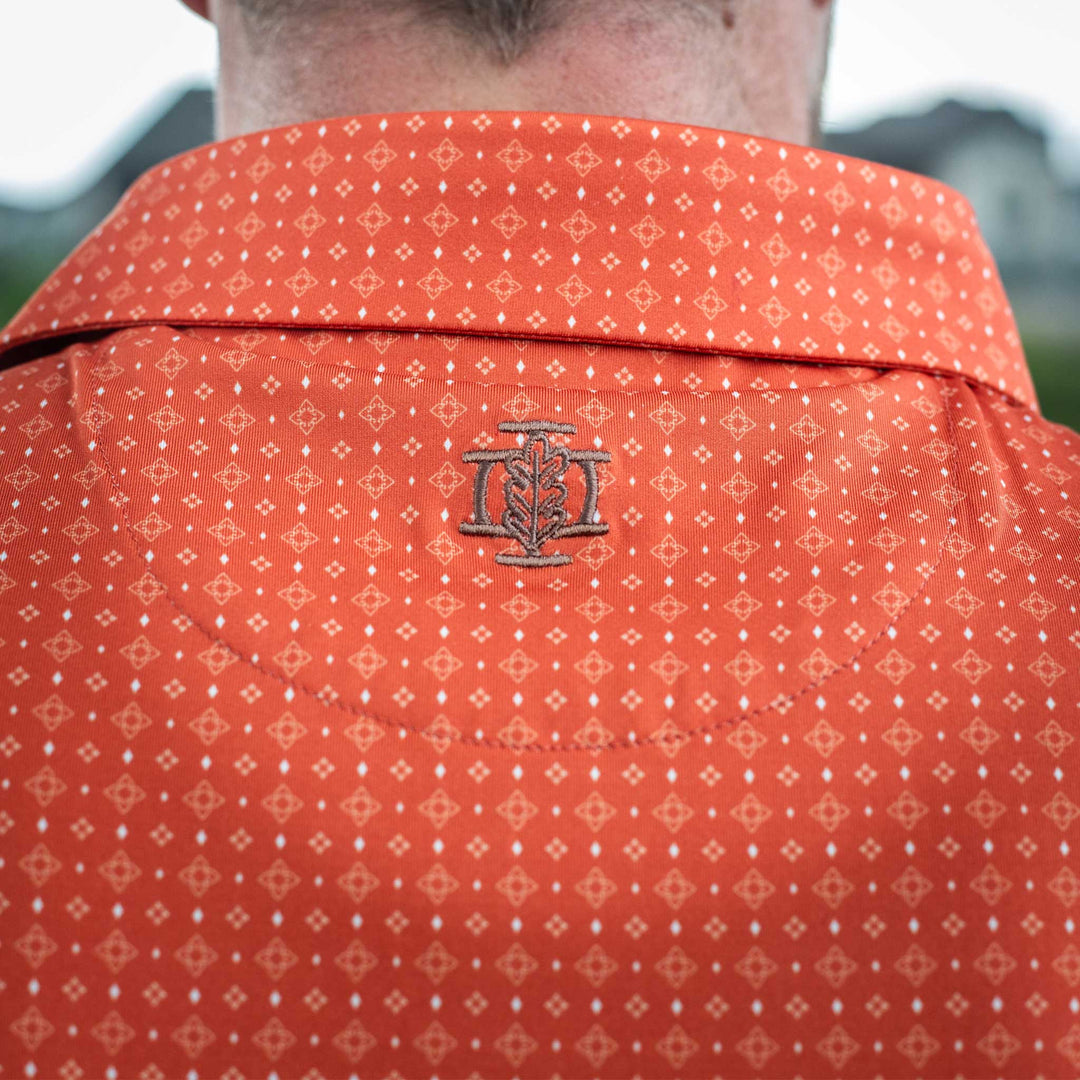 Close-up of the back of The Boone Pearl Snap Polo by Iron Oak Apparel, showcasing a burnt orange western pattern and embroidered logo. This stylish shirt blends modern design with Texan authenticity, perfect for any casual or dressy occasion.
