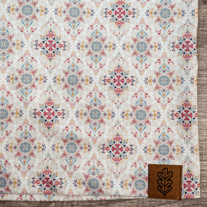 Close-up of the hem of The Classic Pearl Snap Polo by Iron Oak Apparel, showcasing the intricate floral western pattern with vibrant colors and the brand's logo. This stylish shirt blends modern design with Texan authenticity, ideal for any occasion.