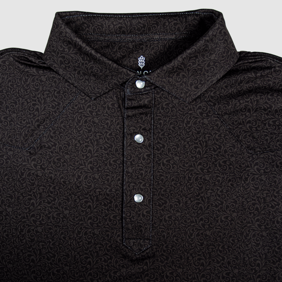 Flat lay of The Folsom Western Yoke Pearl Snap Polo by Iron Oak Apparel, featuring a subtle black paisley Western pattern. The shirt displays signature pearl snap buttons and a stylish collar, perfect for a classic look.