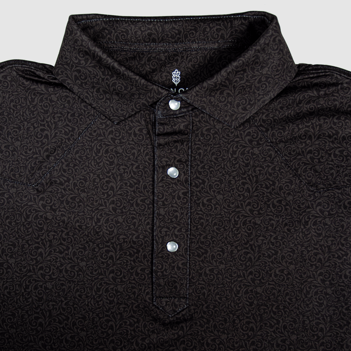 Flat lay of The Folsom Western Yoke Pearl Snap Polo by Iron Oak Apparel, featuring a subtle black paisley Western pattern. The shirt displays signature pearl snap buttons and a stylish collar, perfect for a classic look.