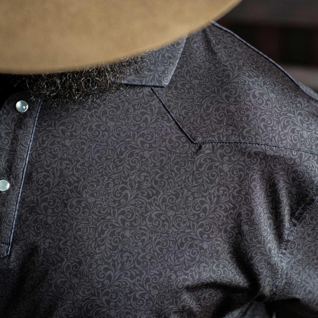 Close-up of The Folsom Western Yoke Pearl Snap Polo by Iron Oak Apparel, highlighting the intricate black paisley Western pattern. The shirt features signature pearl snap buttons, perfect for a classic look.