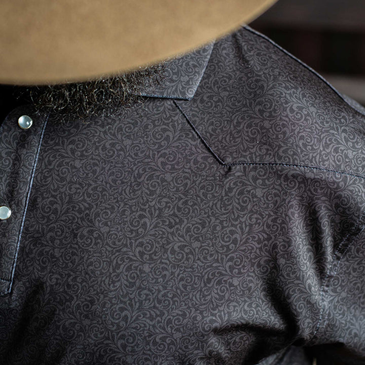 Close-up of The Folsom Western Yoke Pearl Snap Polo by Iron Oak Apparel, highlighting the intricate black paisley Western pattern. The shirt features signature pearl snap buttons, perfect for a classic look.