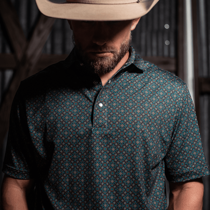 Rugged man in cowboy hat wearing a stylish Pearl Snap Polo by Iron Oak Apparel. The shirt features a unique western pattern, blending Texan roots with modern style. Ideal for casual outings and showcasing authentic Texan fashion.