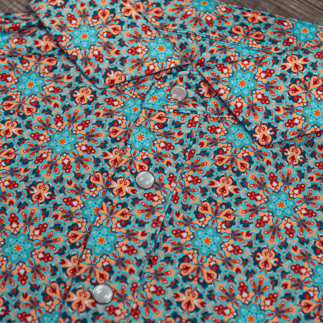 Close-up of The Clementine Pearl Snap Polo by Iron Oak Apparel, featuring a vibrant geometric western pattern with turquoise and orange accents and signature pearl snap buttons. This stylish shirt blends modern design with Texan authenticity, ideal for any occasion.