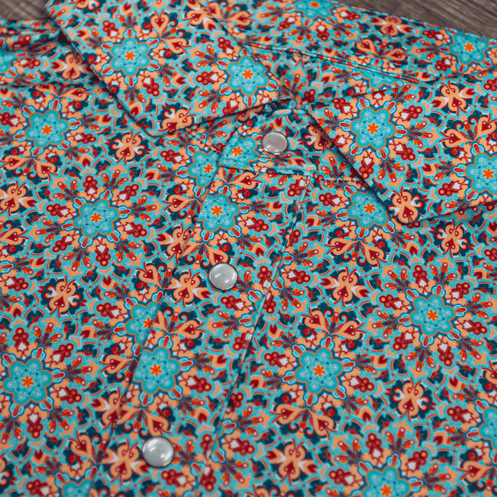 Close-up of The Clementine Pearl Snap Polo by Iron Oak Apparel, featuring a vibrant geometric western pattern with turquoise and orange accents and signature pearl snap buttons. This stylish shirt blends modern design with Texan authenticity, ideal for any occasion.
