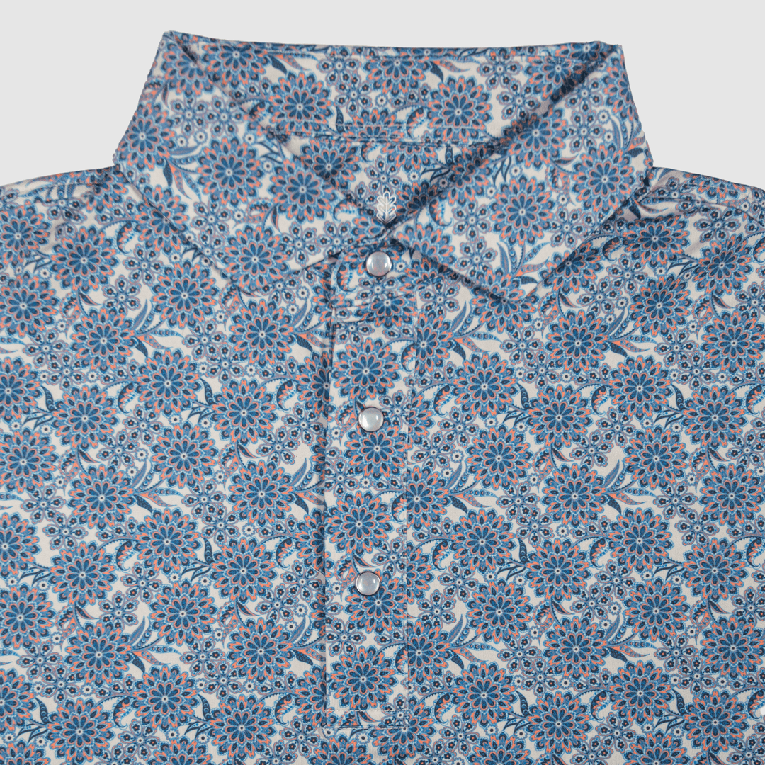 Flat lay of The Gentry Western Yoke Pearl Snap Polo by Iron Oak Apparel, featuring a vibrant blue floral pattern with signature pearl snap buttons and a rigid collar.