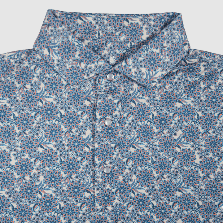 Flat lay of The Gentry Western Yoke Pearl Snap Polo by Iron Oak Apparel, featuring a vibrant blue floral pattern with signature pearl snap buttons and a rigid collar.