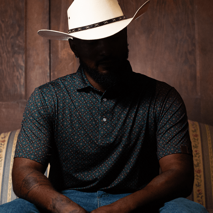 Man wearing a Pearl Snap Polo by Iron Oak Apparel, paired with a white cowboy hat. The shirt's intricate western pattern stands out, embodying modern Texan style and comfort. Perfect for a relaxed, yet sophisticated look.