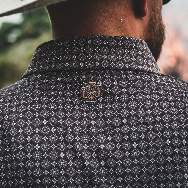 Close-up of the back of The Bandit Pearl Snap Polo by Iron Oak Apparel, featuring a detailed western pattern and embroidered logo. The stylish shirt blends modern design with Texan authenticity, perfect for elevating any casual wardrobe.