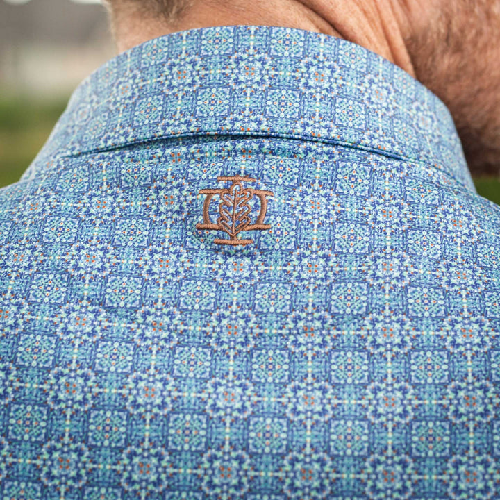 Close-up of the back of The Boot Scoot Pearl Snap Polo by Iron Oak Apparel, featuring a vibrant blue western pattern and embroidered logo. This stylish shirt blends modern design with Texan authenticity, perfect for any casual or dressy occasion.