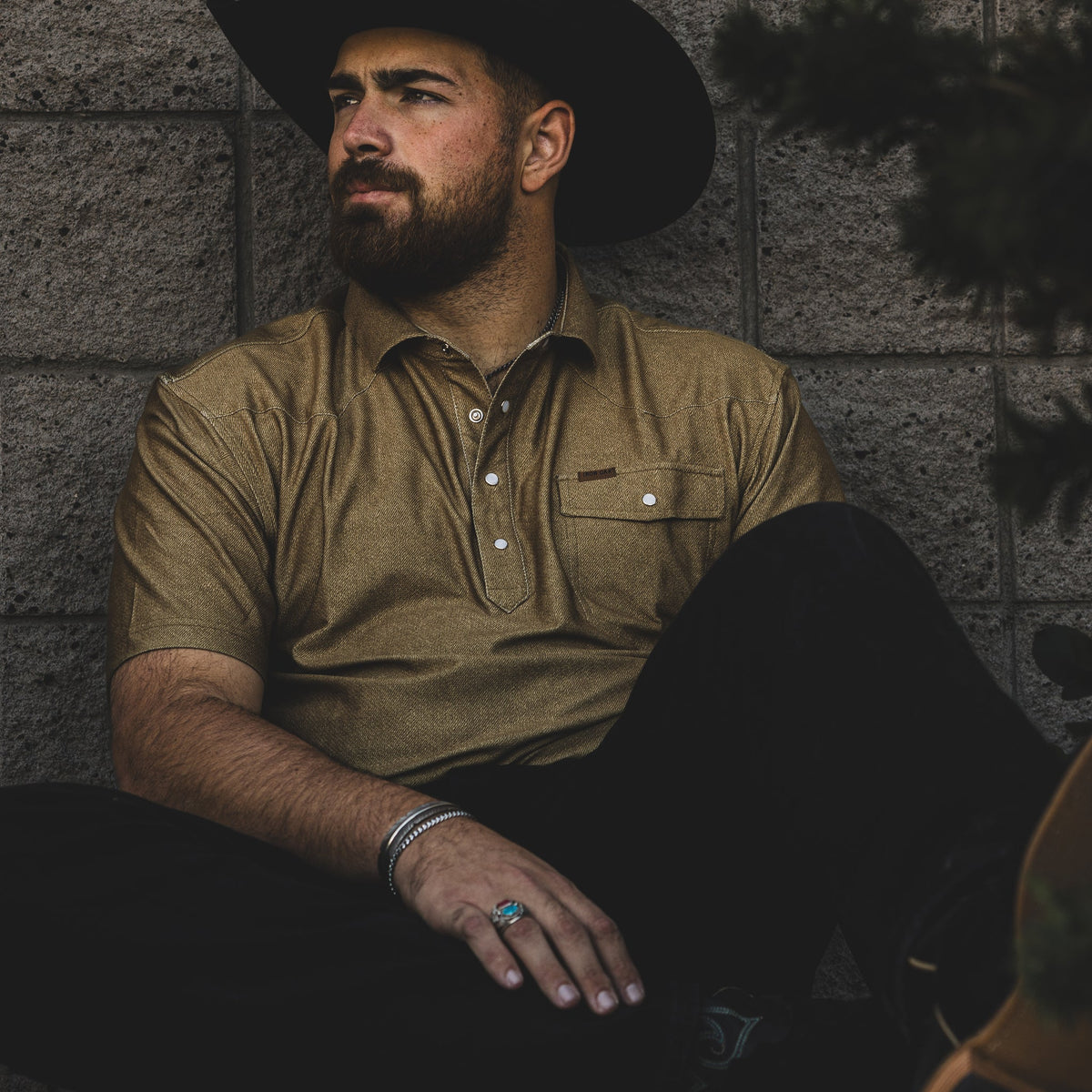 Seated model wearing the Dusty polo with black pants and a cowboy hat