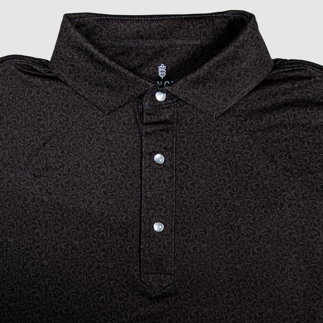  Flat lay of The Folsom Western Yoke Pearl Snap Polo by Iron Oak Apparel, featuring a subtle black paisley Western pattern. The shirt displays signature pearl snap buttons and a stylish collar, perfect for a classic look.