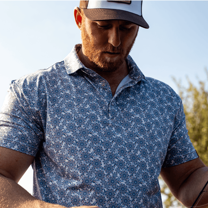 Man wearing The Gentry Western Yoke Pearl Snap Polo by Iron Oak Apparel, highlighting the vibrant blue floral pattern. He stands outdoors, ready for a day of adventure.