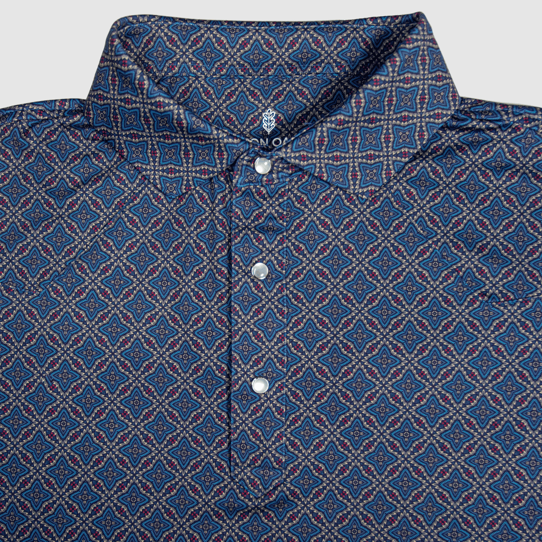  Flat lay of The Granger Western Yoke Pearl Snap Polo by Iron Oak Apparel, featuring a classic blue Western pattern with signature pearl snap buttons and a rigid collar.