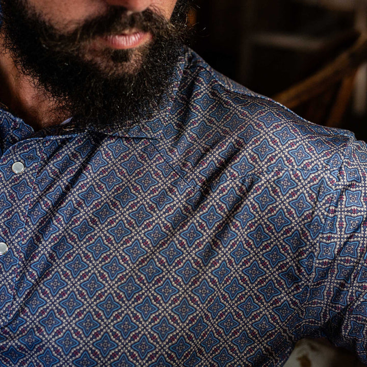 Close-up of The Granger Western Yoke Pearl Snap Polo by Iron Oak Apparel, highlighting the intricate blue Western pattern and the signature pearl snap buttons.