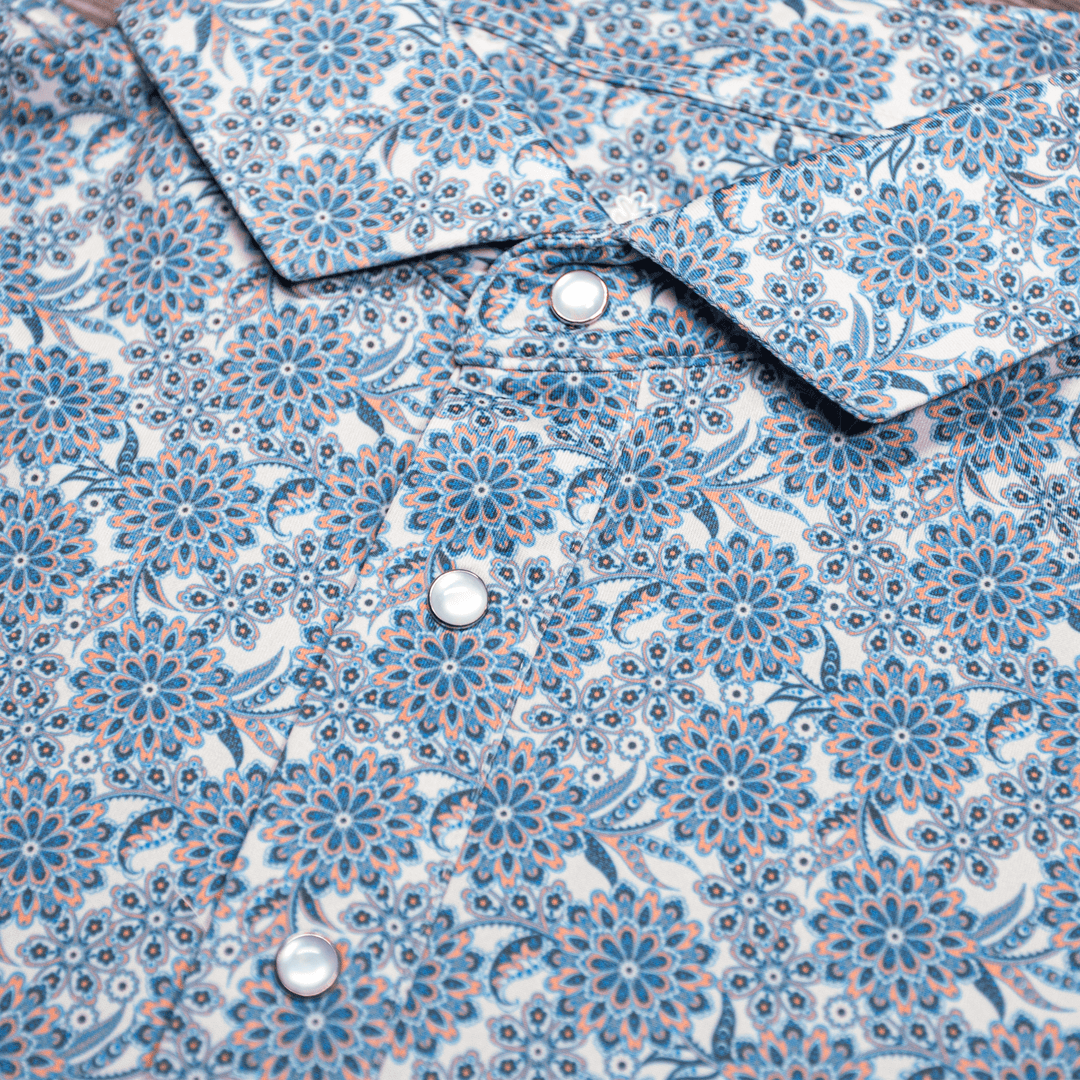 Close-up of The Gentry Western Yoke Pearl Snap Polo by Iron Oak Apparel, highlighting the intricate blue floral pattern and the signature pearl snap buttons.