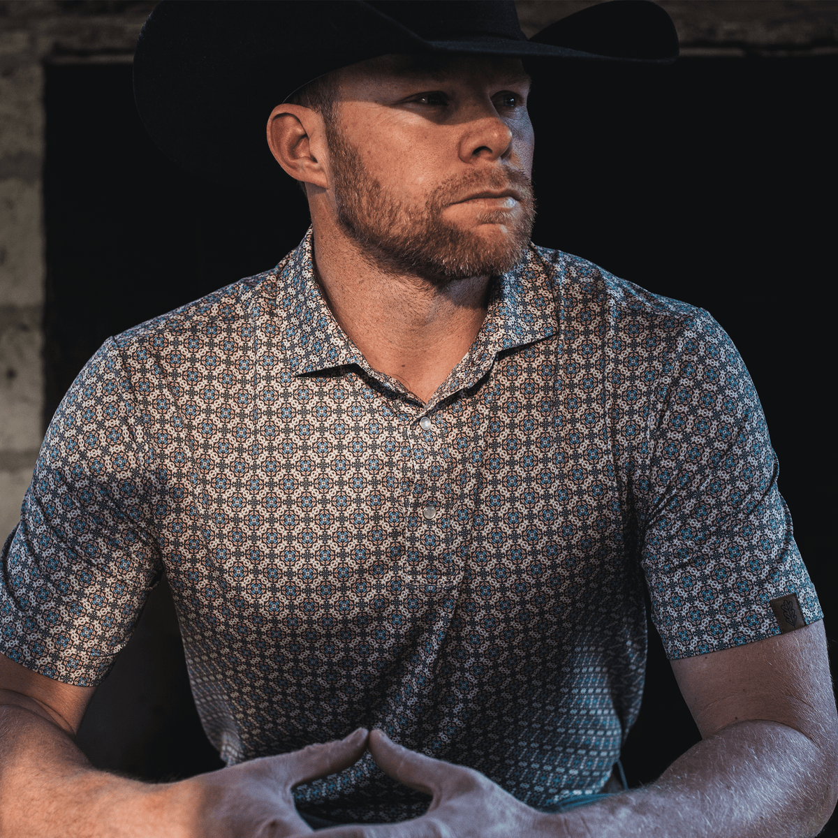 Man wearing The Jaded Pearl Snap Polo by Iron Oak Apparel, exuding confidence and style in a dimly lit setting.